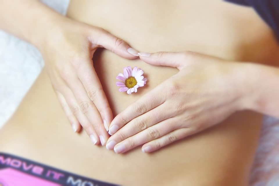Woman laying down with hands framing flower in belly button