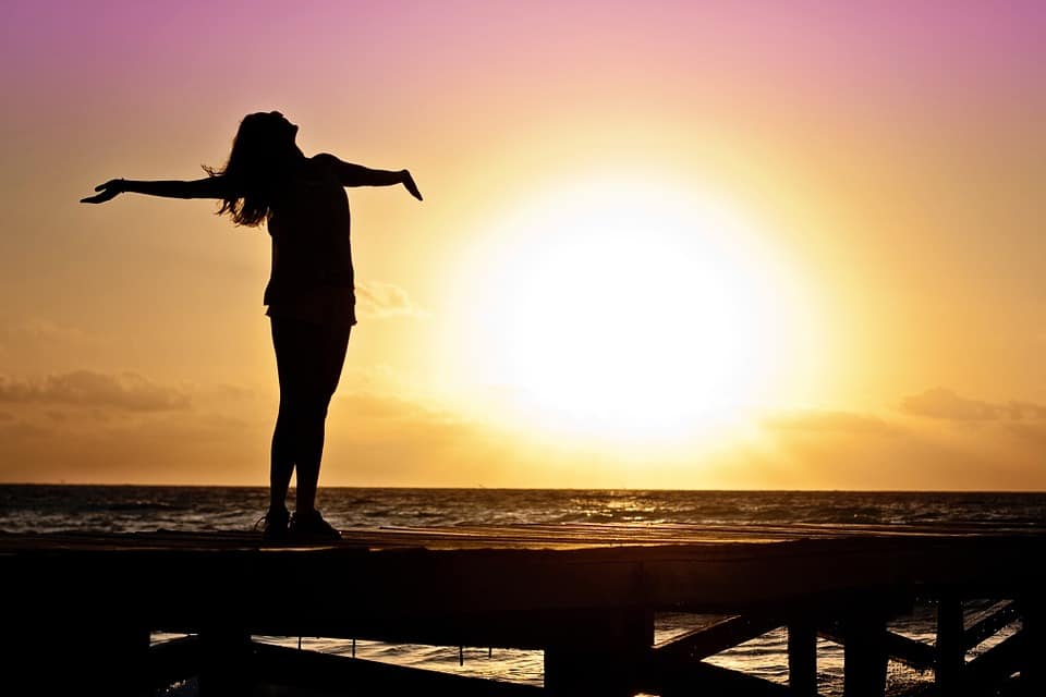 Woman silhouetted in front of sunset with ocean in the background